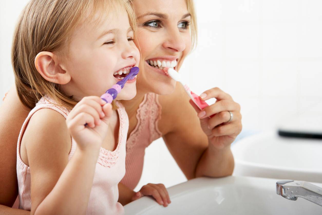 mother helping daughter brush her teeth